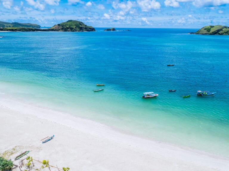 Pantai tersembunyi di Lombok dengan pasir putih dan air laut biru jernih serta beberapa perahu nelayan di tepi pantai